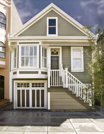 A traditional two-story house with a gabled roof, garage, and front stairs, set against a partly cloudy sky.