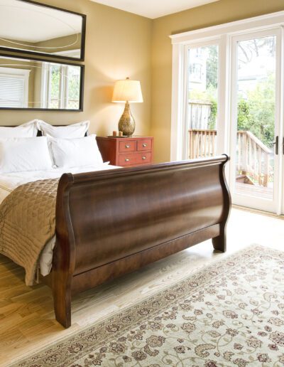 A well-lit, cozy bedroom featuring a wooden sleigh bed, matching bedside tables with lamps, and glass doors leading to an outdoor area.