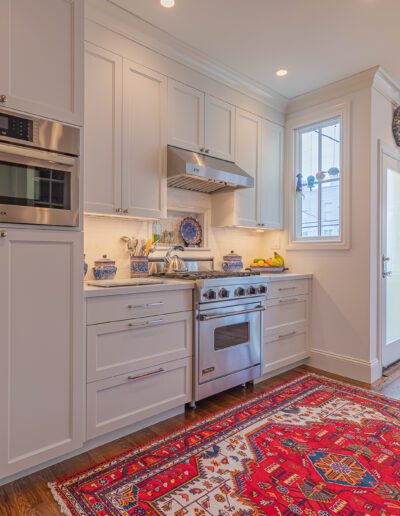 Modern kitchen interior with white cabinetry, stainless steel appliances, and a red patterned rug.