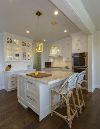 Modern kitchen interior with white cabinetry, stainless steel appliances, and a central island with bar stools.