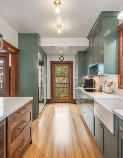 Bright, modern kitchen with white countertops, teal cabinets, and wooden accents. large windows provide natural light, and a door leads to an outdoor balcony.