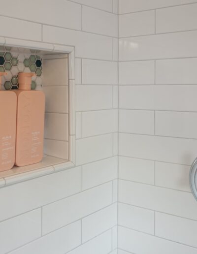 Modern shower niche with shampoo and conditioner bottles next to a chrome shower control valve in a white tiled wall.