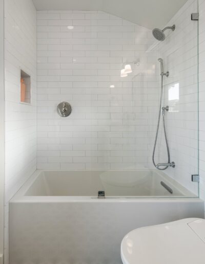 Modern bathroom featuring a white bathtub with overhead shower, surrounded by white subway tiles, and a floor with black and green mosaic tiles.